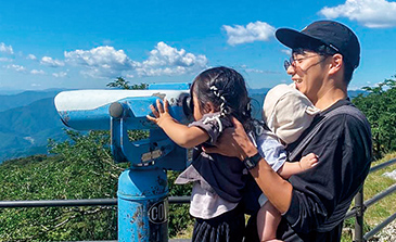 望遠鏡をのぞき込んでいる女の子を赤ちゃんを抱えたお父さんが支えている様子