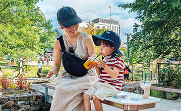 ベンチに座ってシュースを飲む子どもとお母さんの写真