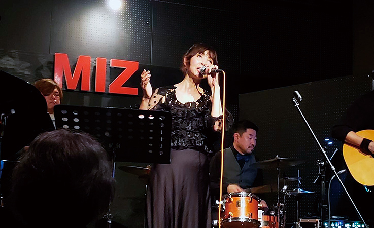 バンドとともにステージで歌唱する小島さんの写真